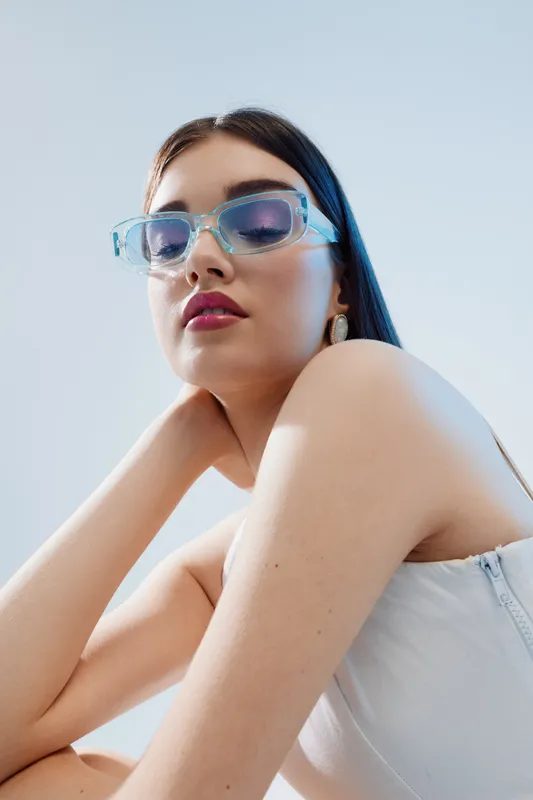 Young woman wearing stylish transparent sunglasses poses confidently against a light background. Concept of beauty fashion, style, and modern accessories for women.