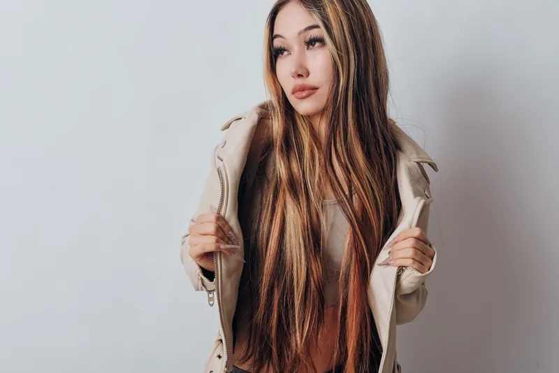 Young woman with long straight hair wearing beige jacket and neutral expression on white background. Beauty portrait of female model in casual stylish outerwear for fashion.