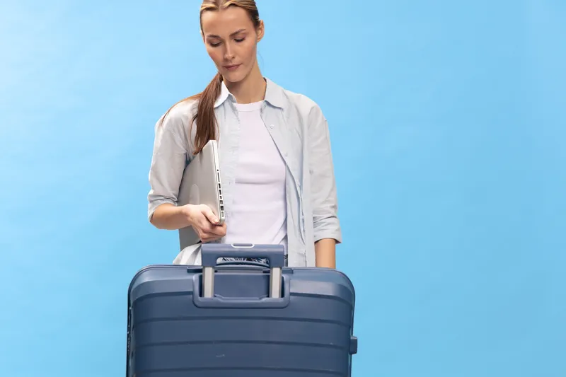 Young woman with suitcase on blue background prepares for travel. She looks focused and ready, wearing casual clothes. Concept of vacation, journey, packing, and lifestyle.