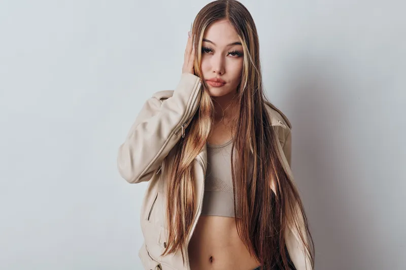 Young woman with long hair and casual beige jacket posing in studio with neutral background. Fashion model with natural makeup and relaxed facial expression looking at camera.