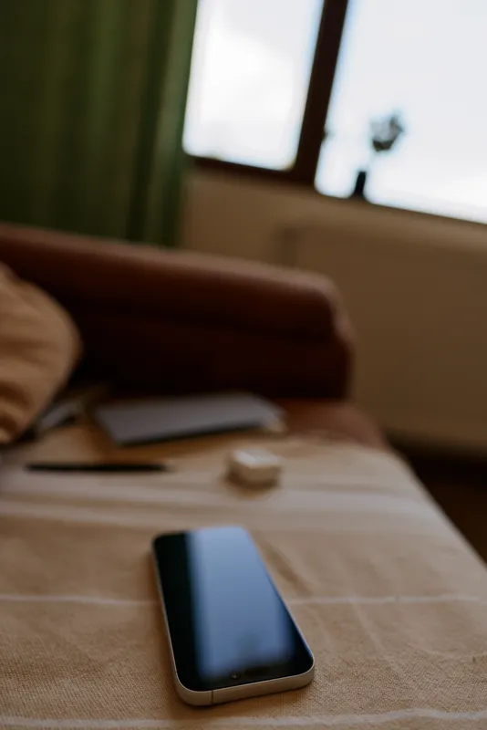 A modern living room scene shows a smartphone resting on a striped table in front of a couch and a window, capturing a calm, everyday moment of home life.