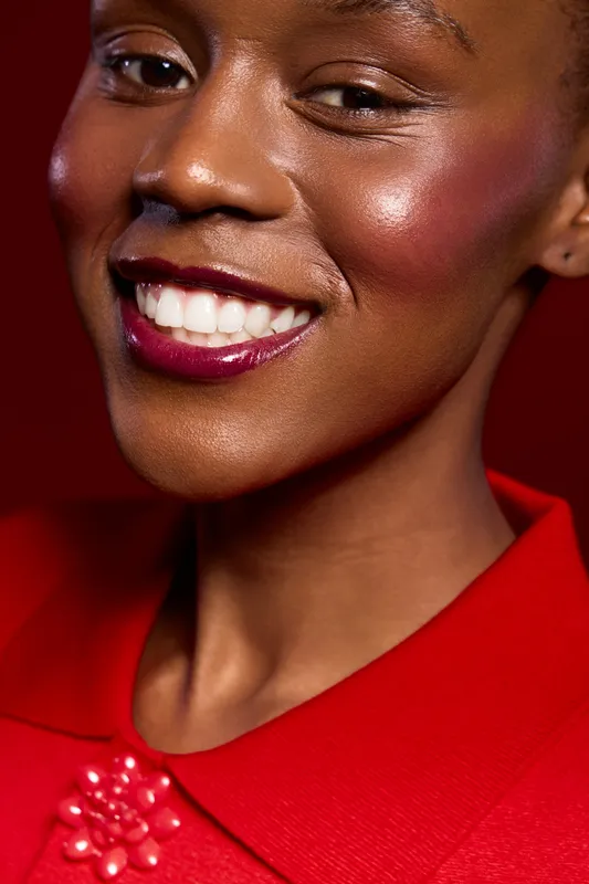 Close-up of a smiling black woman with dark skin wearing red lipstick and a red top. The image highlights beauty, confidence, and elegance with vibrant red tones and natural makeup.