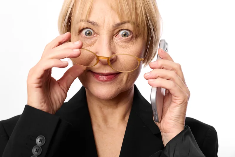 Older woman phone paper mustache surprised studio portrait, holding phone to ear, suit jacket, playful prank face, white background close up smiling