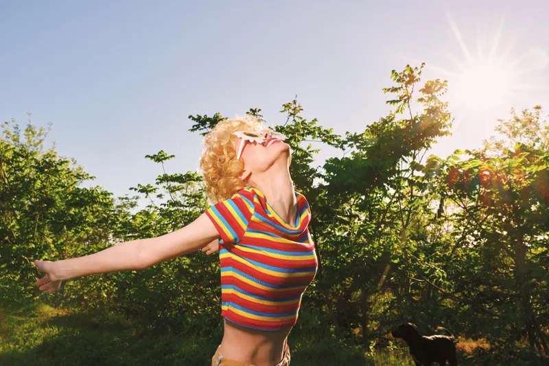 Joyful woman outdoor sunshine joy summer colorful retro candid lifestyle portrait in a sunlit garden, arms outstretched, carefree mood and vibrant light, natural breeze and open space