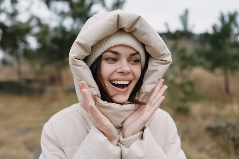 Girl in a hooded warm jacket outdoors in winter, smiling with joy, cozy scene with soft textures and bright expression against a simple natural landscape and open terrain