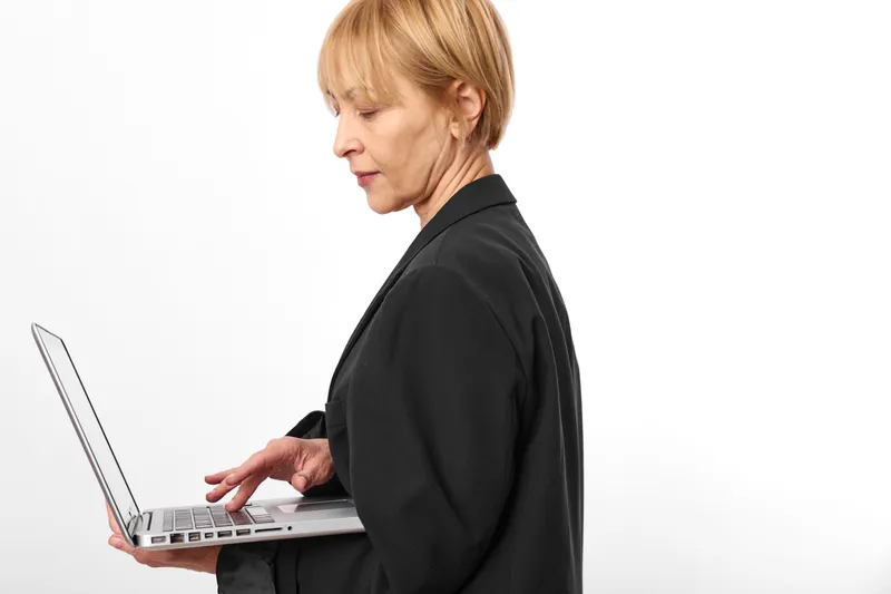Senior businesswoman typing on a laptop in profile, focused expression, isolated on white studio background, modern technology concept for remote work and communication