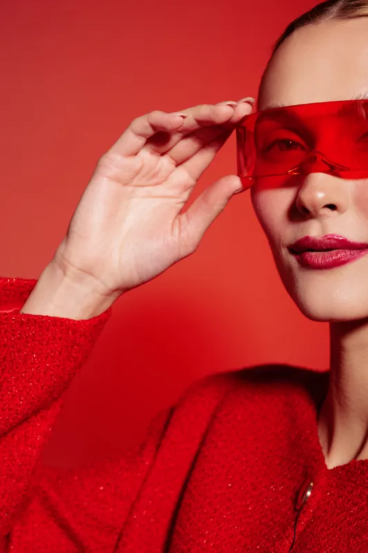 Close-up of a woman wearing red sunglasses and a red sweater against a red background. Fashion portrait with vibrant colors and modern style concept.