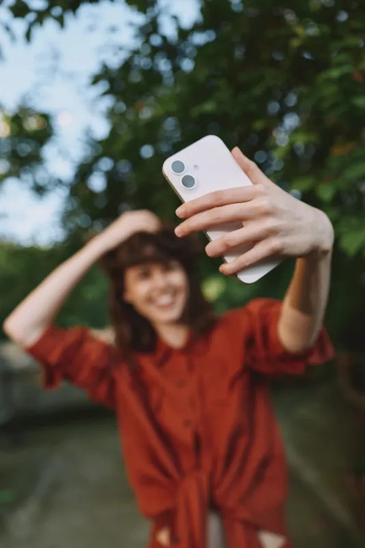 Candid woman lifestyle shot: a smiling woman takes a selfie outdoors in a park, wearing a red dress, capturing a joyful moment and sunny, relaxed atmosphere