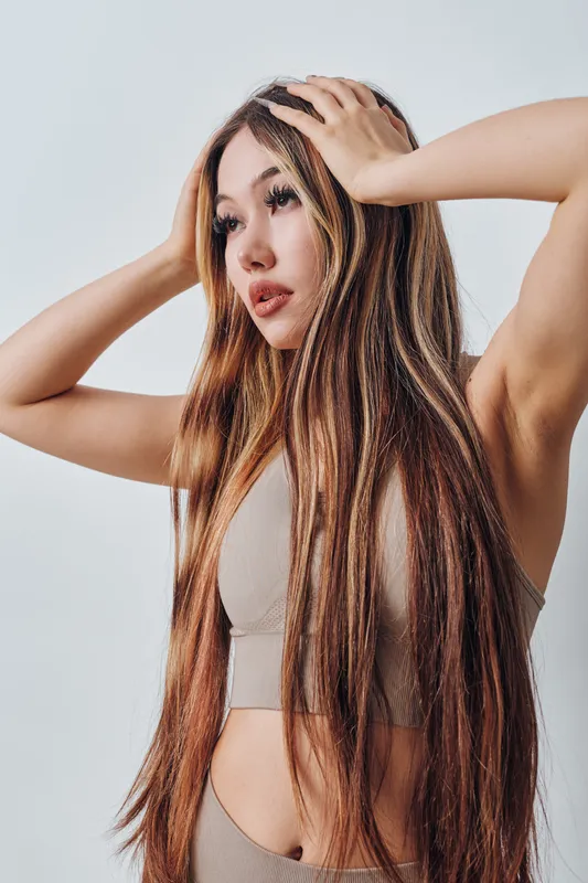 Young woman with long hair wearing beige sportswear posing with hands on head, isolated on white background for fitness or beauty concept and lifestyle portrait.