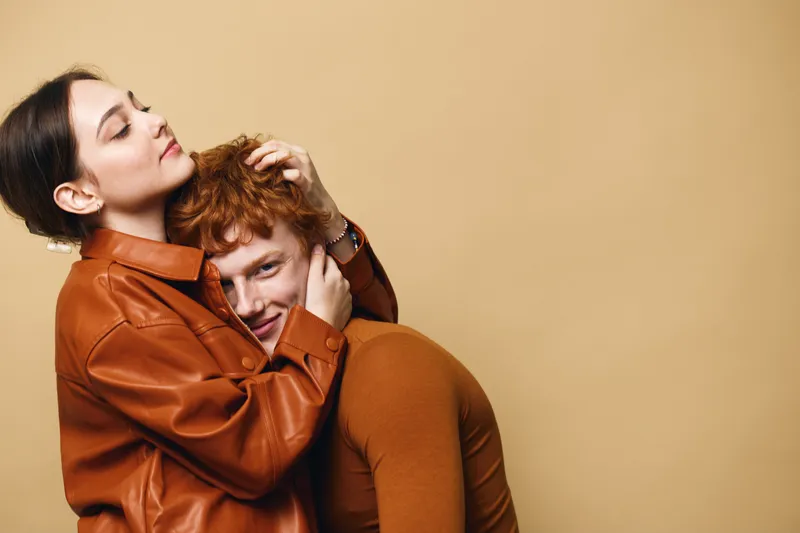 Couple in love with warm embrace, woman and man in casual clothing on beige background. Romantic moment with affection and happiness between young partners.