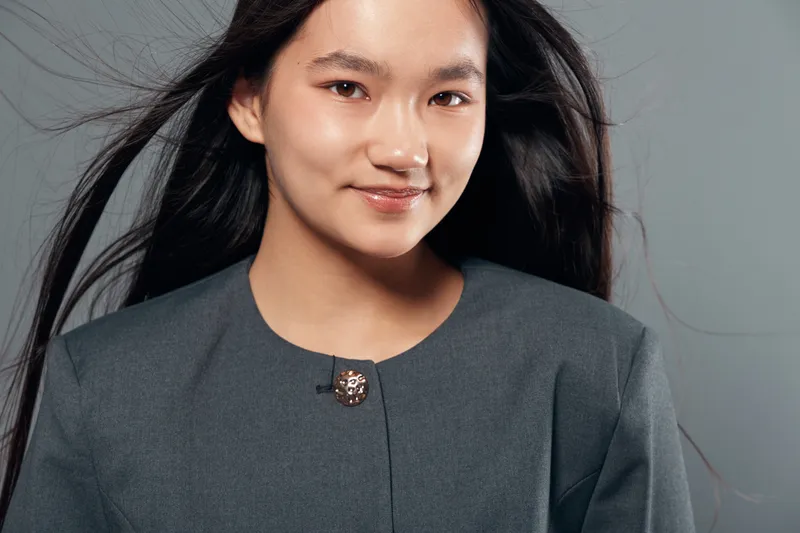 Woman portrait, smiling young asian female with long black hair wearing grey jacket standing against plain background, confident and professional look for business or lifestyle.