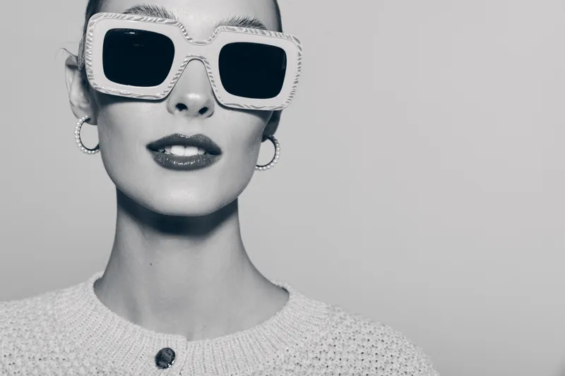 Stylish white woman with fair skin wearing large square sunglasses and hoop earrings in a close-up black and white portrait.
