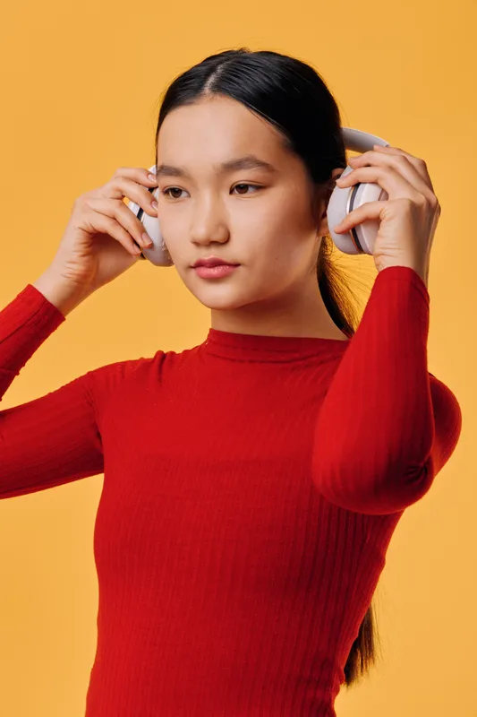Young woman with headphones wearing red sweater on orange background posing for music listening, technology, entertainment and lifestyle portrait with copyspace for sound or audio concept.
