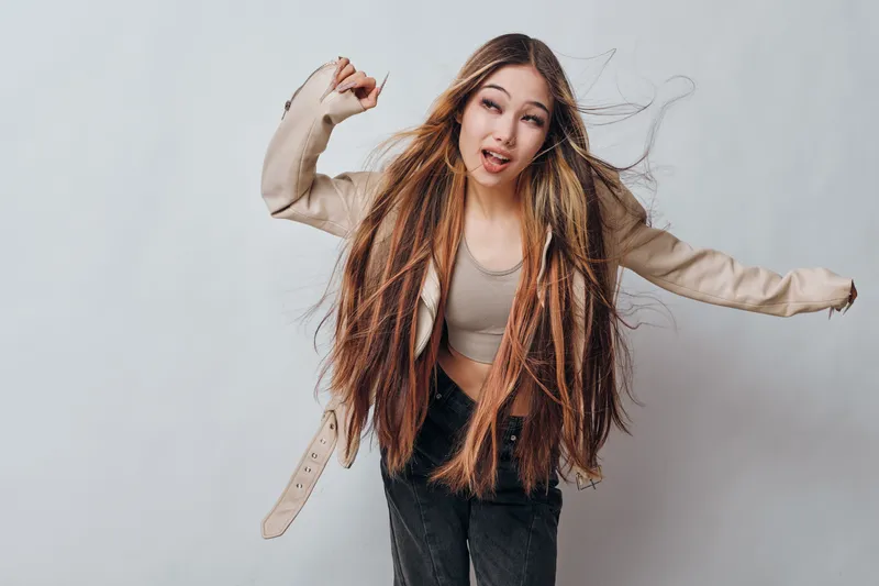 Young woman with long dreadlocks and casual outfit dancing and enjoying herself on plain background. Movement, hairstyle and joyful expression in studio with natural look.