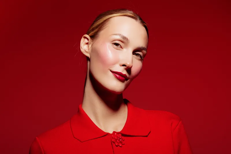 Portrait of confident woman with red lipstick and red outfit on red background. Studio lighting highlights her smooth skin and elegant expression. Concept of beauty and fashion.
