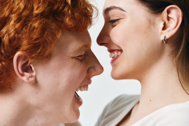 Couple, young man and woman smiling close together with happy faces in love and intimacy with casual clothing and natural light on white background.