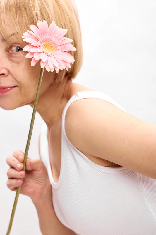 Woman older, pink gerbera flower, holding stem in closeup, face near camera, gentle smile, spring beauty mood, isolated on white studio background