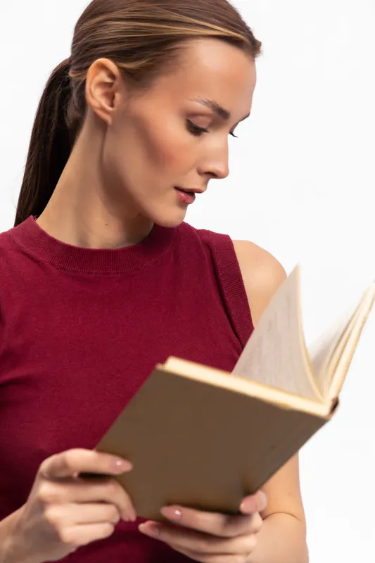 Young woman in red sleeveless top reads book with focus and interest isolated on white background. Concept of education, learning, and concentration in casual lifestyle.