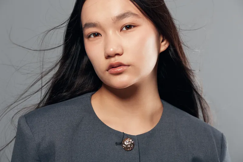 Portrait of young woman with long hair wearing gray jacket on gray background looking at camera with neutral expression and natural makeup for beauty and fashion concept.