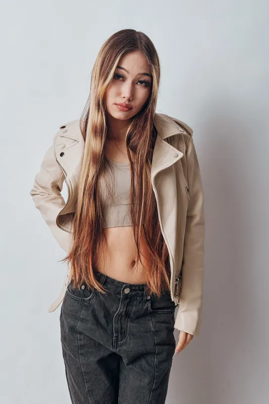 Young woman with long hair wearing casual crop top and light jacket posing against white background in studio, fashion portrait with confident expression.