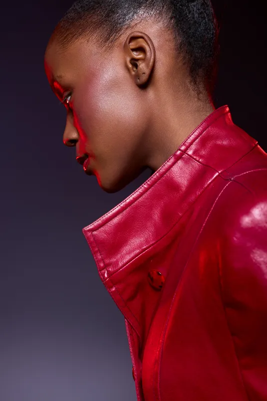 Profile of a serious African woman with dark skin wearing a red leather jacket. Studio portrait with dramatic lighting and purple background. Concept of fashion, style, and confidence.