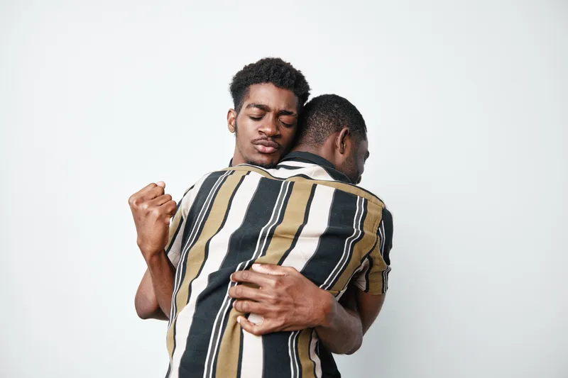 Two young black men hugging each other with closed eyes and emotional connection on white background. Friendship, support and affection between african american males.