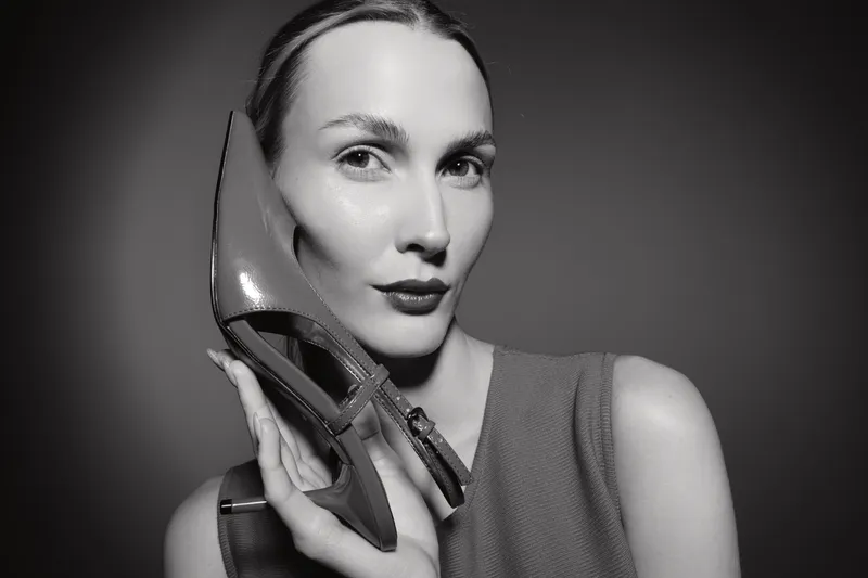 Young white woman with pale skin holds a high heel shoe near her face in a stylish monochrome portrait. Concept of fashion and elegance.