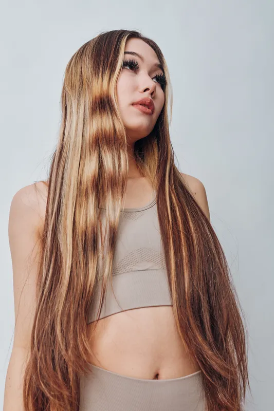 Young woman with long straight hair wearing beige crop top standing with neutral expression against plain background in studio environment. Beauty, fashion and style concept.