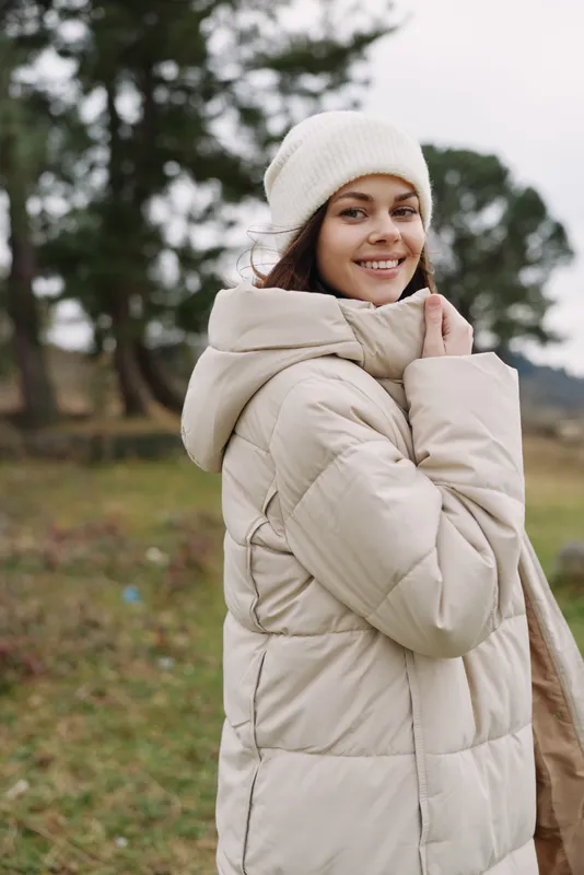Woman wearing a beige puffer coat in an outdoor park setting, winter calm, smiling in a cozy jacket and scarf, natural light, candid portrait for lifestyle fashion and warmth