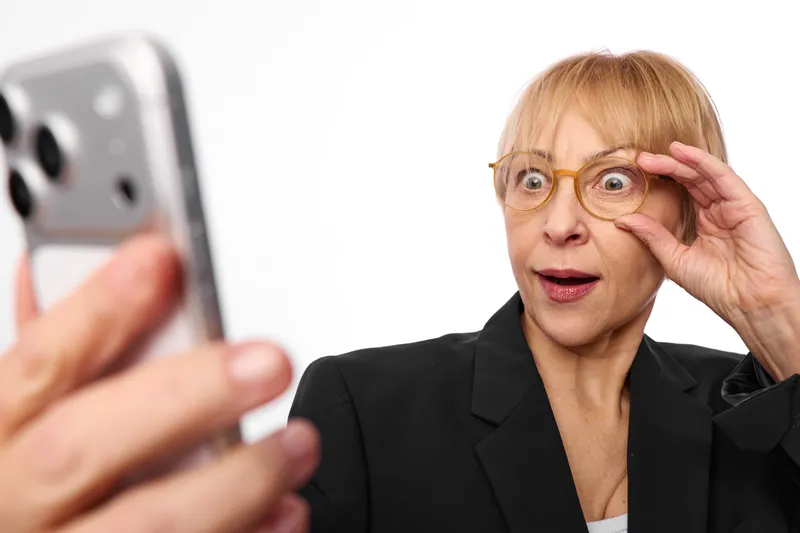 Business woman adjusting glasses frames, surprised look, hand and smartphone nearby, close up portrait, modern office technology, soft light, shallow depth