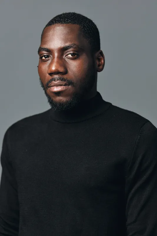 African man portrait with beard wearing black turtleneck sweater in creative conceptual visual style studio background. Confident male model with serious expression and short hair.
