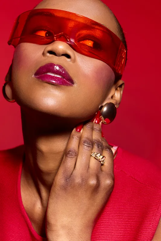 Close-up portrait of a stylish dark skinned African woman with shaved head wearing red translucent glasses and red outfit. Concept for fashion, beauty, accessories, and confidence.