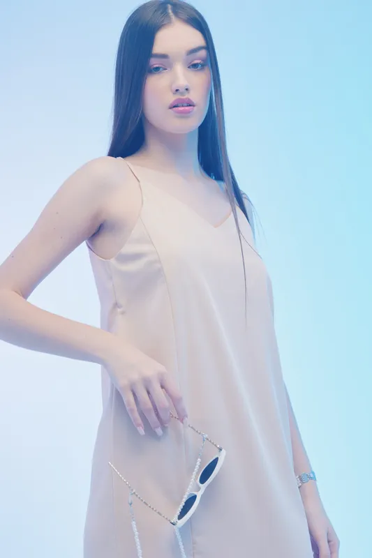 Young woman with long straight hair wearing a beige dress holds sunglasses in hand. Soft blue background highlights beauty and fashion concept.