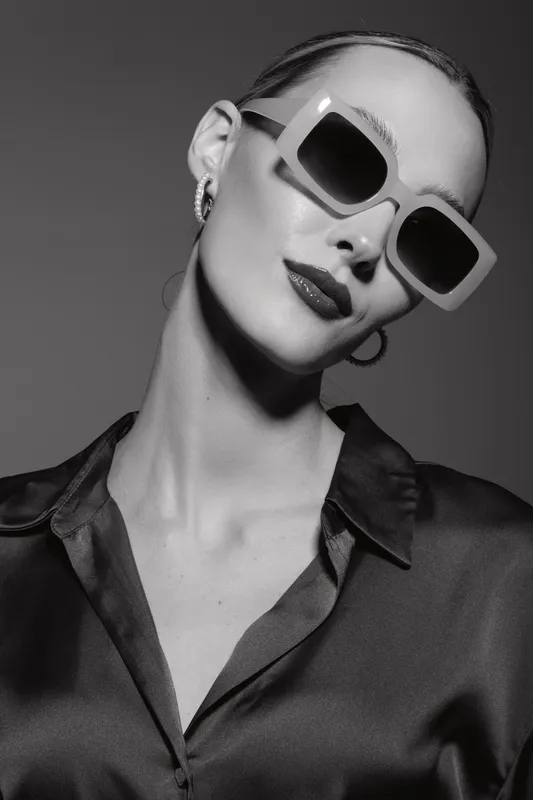 Stylish white woman with pale skin wearing large sunglasses and satin blouse posing confidently in studio portrait. Fashion and elegance concept.