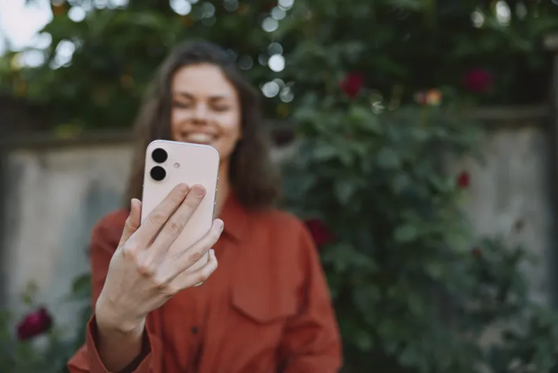 Young woman enjoying outdoor lifestyle, taking a selfie with smartphone among blooming roses, casual fashion, joyful mood, candid portrait in garden bright natural light