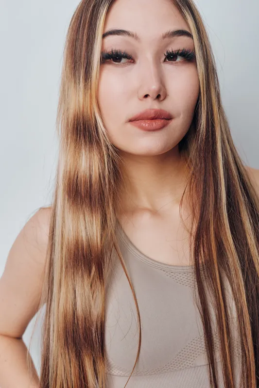 Portrait of a young woman with long straight hair wearing a sleeveless top with natural makeup and neutral expression on gray background for beauty or fashion.
