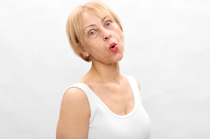Surprised elderly woman, shocked open mouth face, looking toward camera, portrait on clean white background, expressive emotion, studio minimal composition.