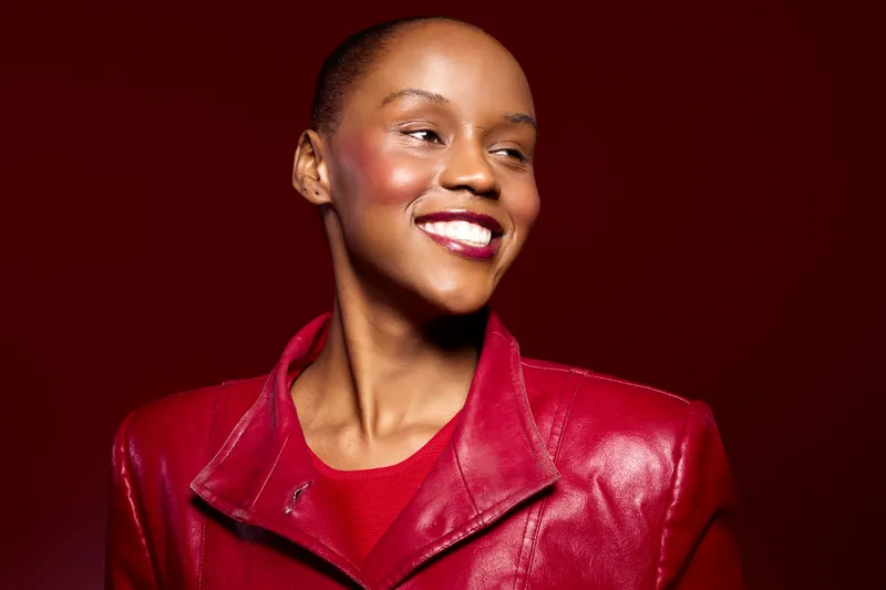 Smiling African American woman with dark skin wearing a red leather jacket and red top. Studio portrait on a red background. Concept of confidence, fashion, and beauty with vibrant colors.