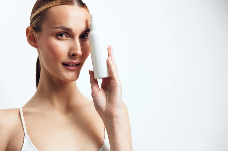 Young woman applying skincare cream from tube on face, holding beauty product for self care, hygiene routine, soft studio light, minimal background, close up portrait