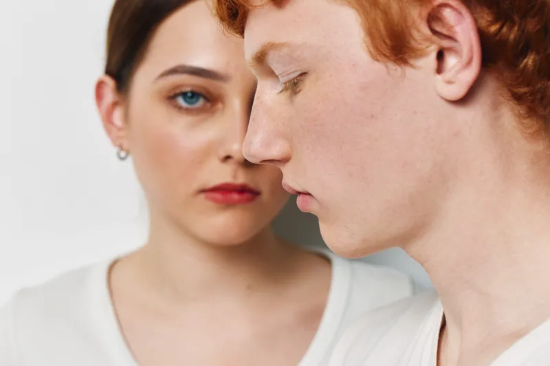 Portrait of young man and woman with serious expressions on white background in studio. Closeup of two people with natural skin tones and minimal makeup in casual clothing.