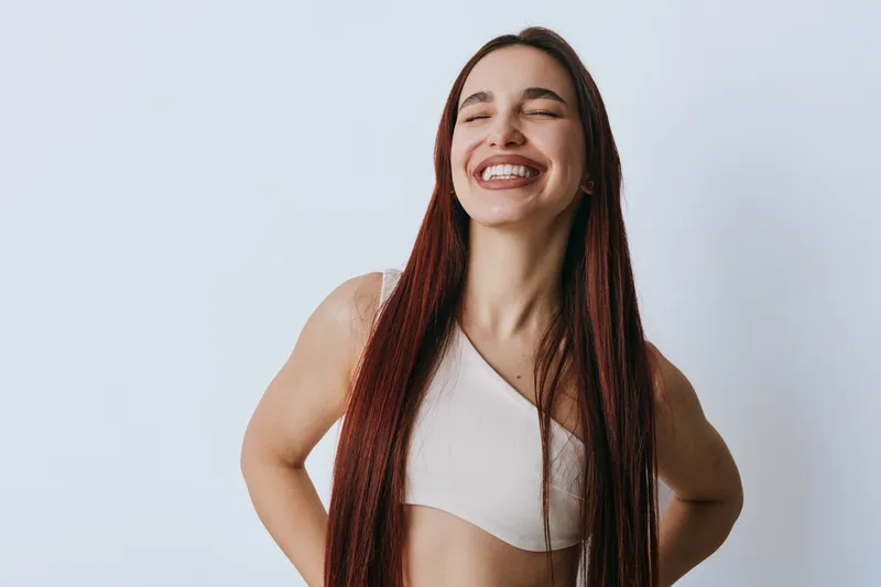 Young woman with long braided hair smiling with closed eyes in casual top against white background. Portrait of happy female with natural look and relaxed pose.
