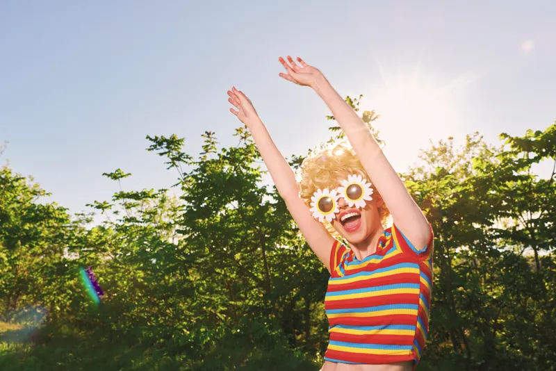 Woman with flower sunglasses wears a striped shirt, enjoying a sunny outdoor moment, candid lifestyle shot with retro film color, bright greenery and joyful mood, energetic sense of summer.