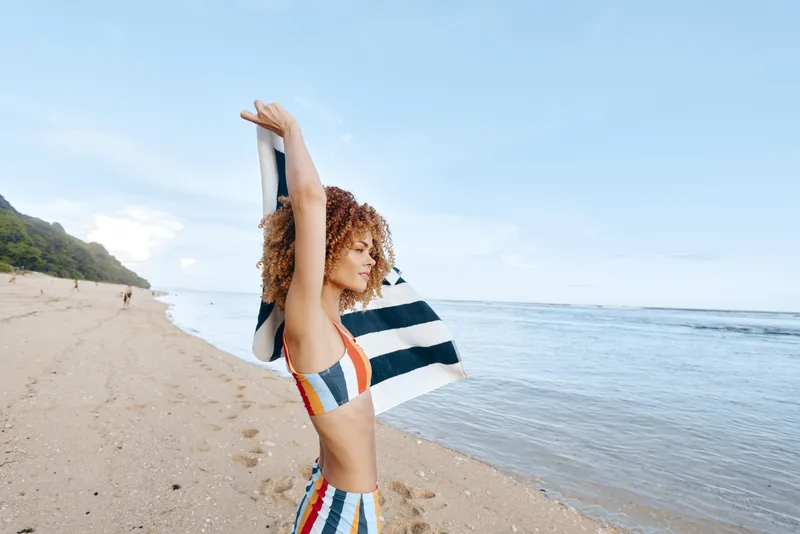 Woman beach seaside summer stretching vacation lifestyle relaxation, smiling woman stretches arms on sand by the ocean, waves and bright sky create a peaceful seaside getaway today