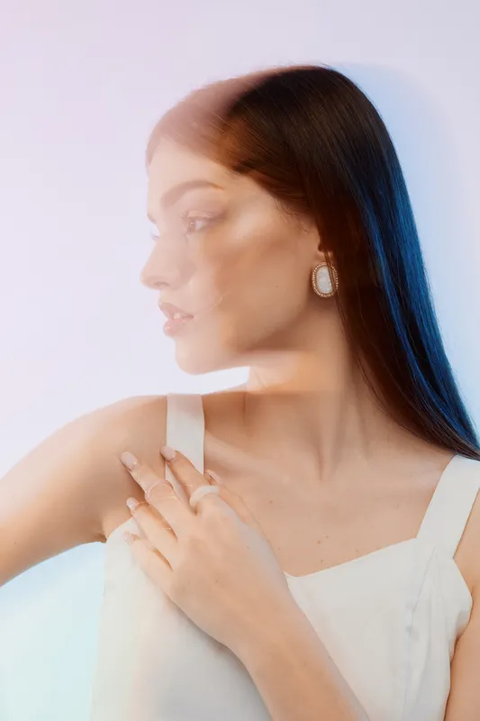 Portrait of a young woman with long hair wearing white top and earrings. Soft lighting and blurred double exposure effect create a dreamy beauty and fashion concept.