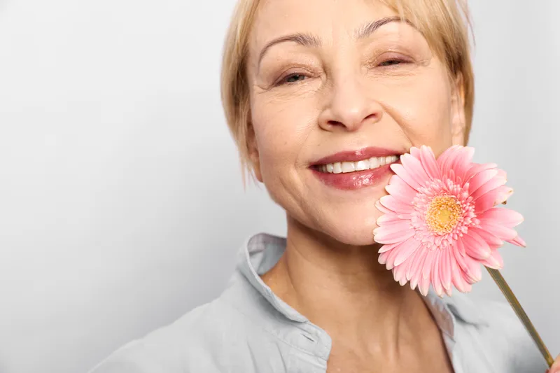Woman smiling pink flower senior closeup portrait, beauty skincare wellness concept, face skin care, soft studio light on white background, happy gentle calm mood