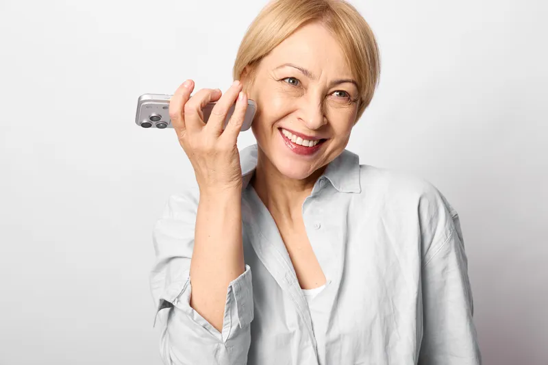 Elderly woman smiling answers a smartphone call in an indoor portrait, friendly communication with wireless technology. Senior wellbeing concept about connection, voice, and trust