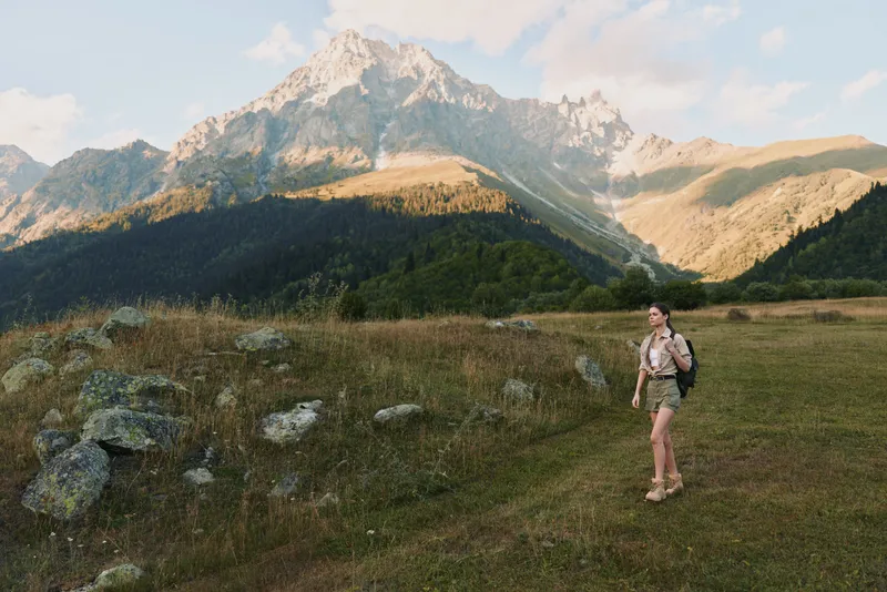 Woman hiking in a mountain landscape, outdoor lifestyle scene with backpack, rugged terrain, blue sky, and distant peaks, conveying adventure, exploration, and nature immersion.