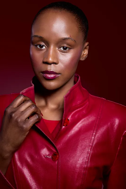 Portrait of confident black woman with dark skin wearing red leather jacket and shirt. Studio shot on dark red background. Concept of fashion, beauty, and elegance.