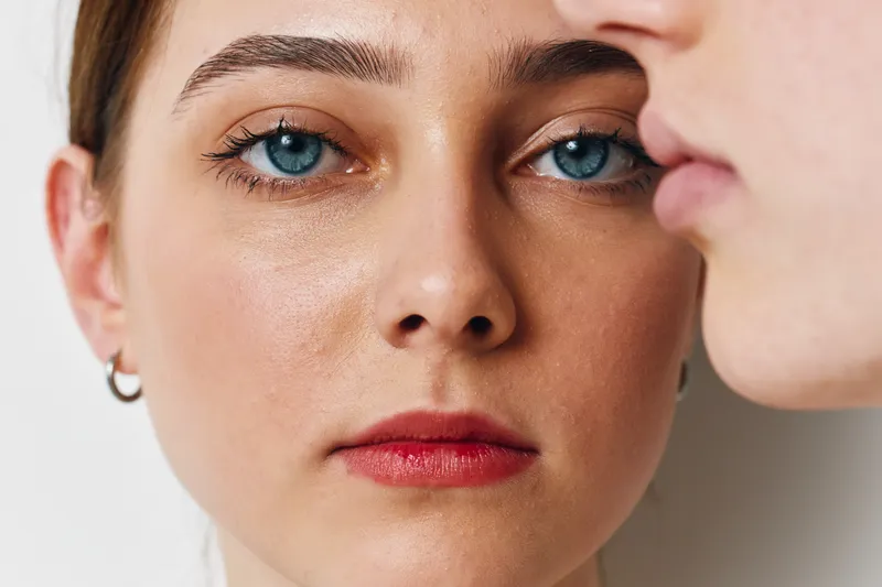 Close up portrait of young woman with blue eyes and red lips looking at camera with serious expression against white background. Beauty, skin, face details.