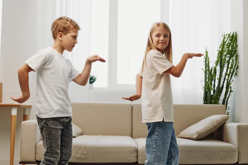 Two children playing indoors, boy and girl mimicking karate poses in casual clothes in bright living room. Concept of childhood fun, family activity, and healthy lifestyle.